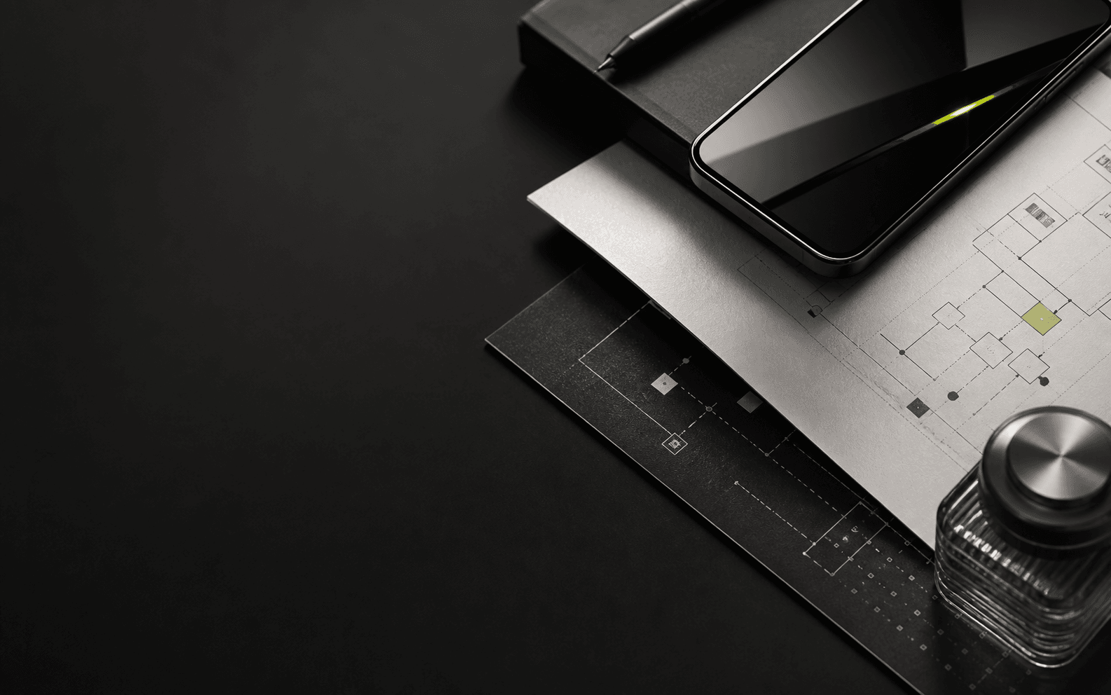 Dark product engineering workbench with a phone, architecture papers, and graphite desk materials
