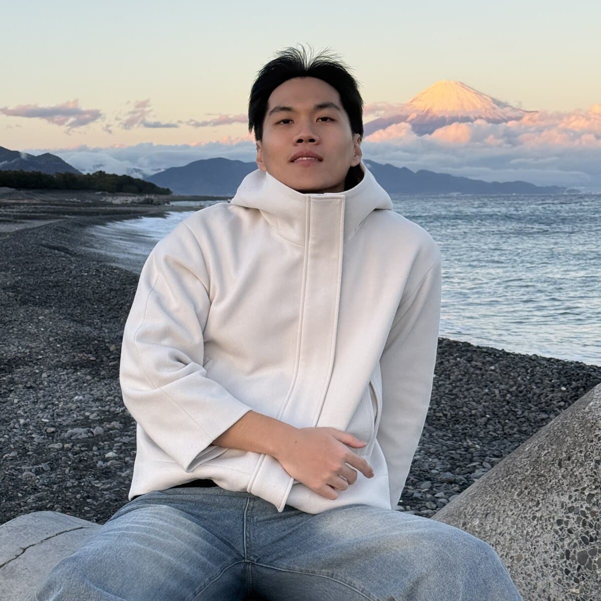 Kan sitting on the rocks at the beach at dusk, Mount Fuji behind him.